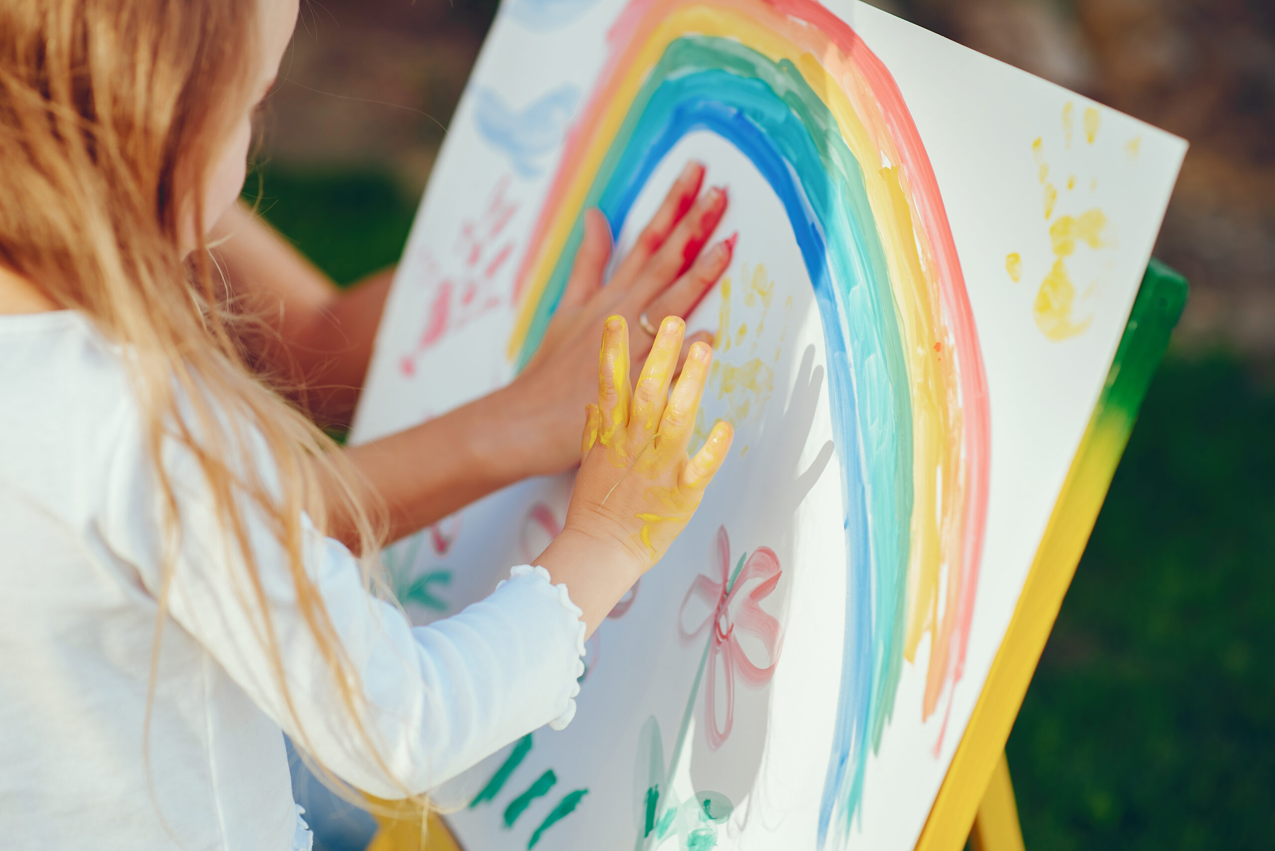 Beauty mother paint with her little daughter. Stylish woman drawing the picture with little girl. Cute kid in a white t-shirt and blue jeans